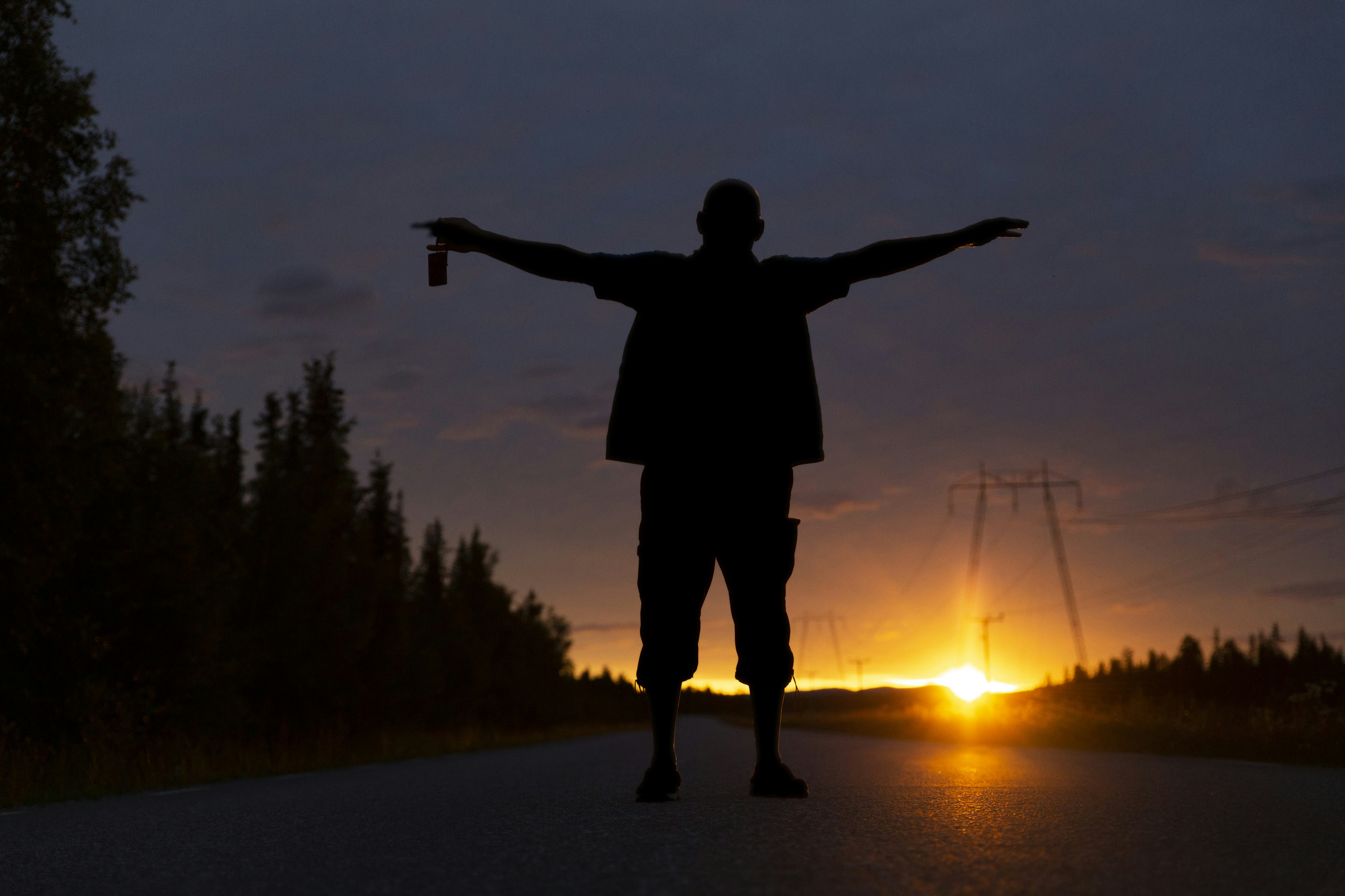 silhouette of man standing on road during sunset, A photo of my father posing in front of the midnight sun in the northern parts of Sweden. The photo is taken a few minutes after midnight.