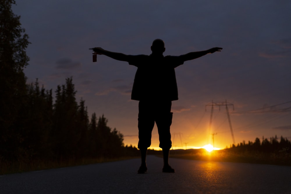 silhouette of man standing on road during sunset