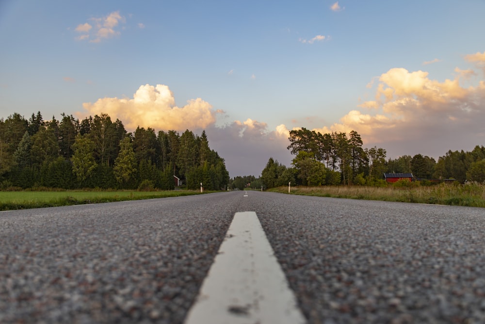 gray concrete road between green trees under white clouds and blue sky during daytime