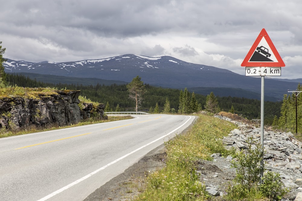 gray asphalt road near green grass field and mountain during daytime