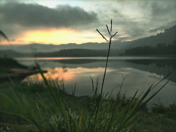 A serene landscape with a person meditating by a calm lake at sunrise.