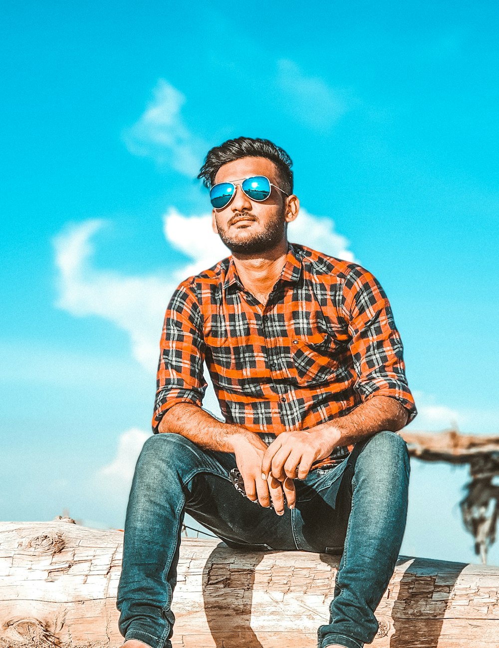 man in red white and blue plaid dress shirt and blue denim jeans sitting on brown