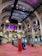 The interior of a large, ornately designed building with arched ceilings and intricate architectural details. The space features gaming machines lined up along the floor, under a high ceiling with a grid pattern. Lighting in purple and white tones enhances the ambiance.