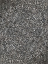 A close-up view of textured asphalt road surface with visible rough and bumpy aggregate particles. The image captures the gritty details and uneven nature of the asphalt material.