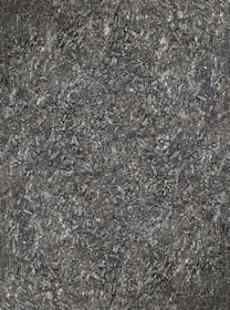A close-up view of textured asphalt road surface with visible rough and bumpy aggregate particles. The image captures the gritty details and uneven nature of the asphalt material.