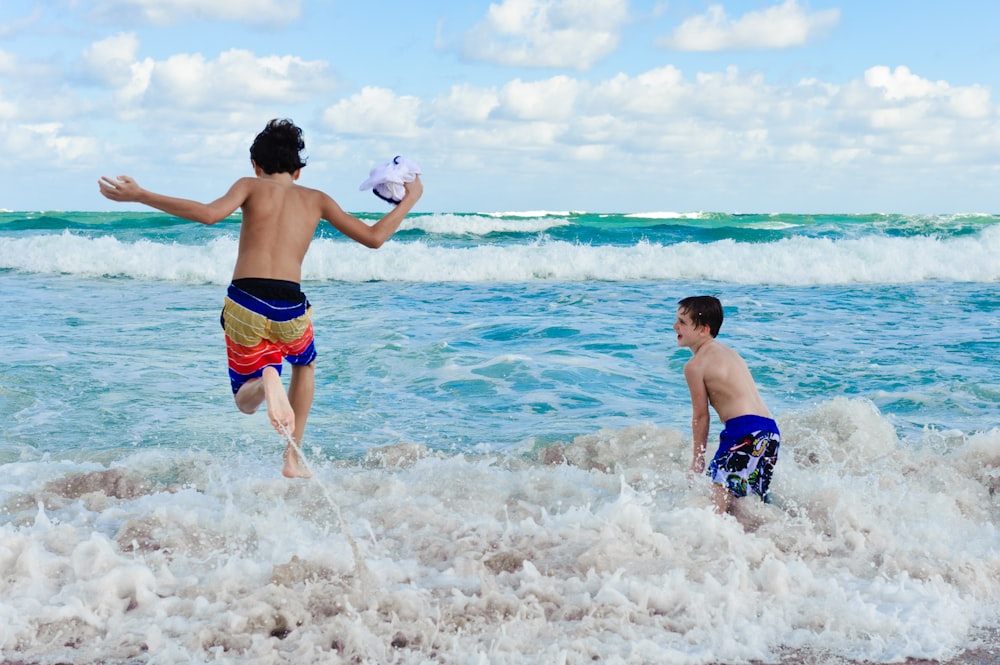 2 boys in blue shorts running on beach during daytime