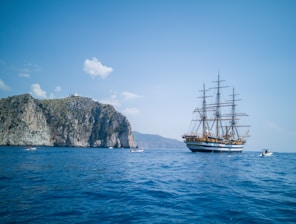 brown ship on sea near mountain under blue sky during daytime