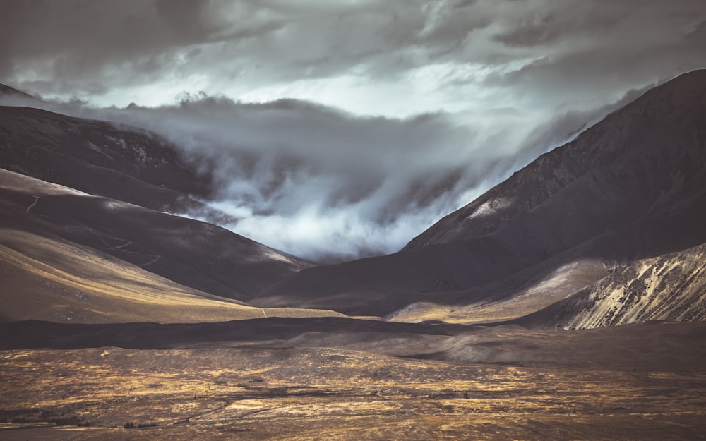 brown field near mountain under cloudy sky during daytime