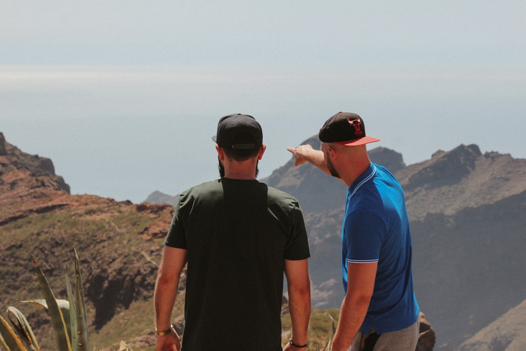 2 men in black t-shirt standing on brown rock formation during daytime