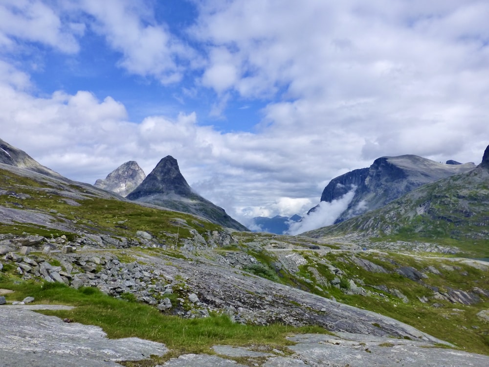 green grass field near mountain under white clouds and blue sky during daytime