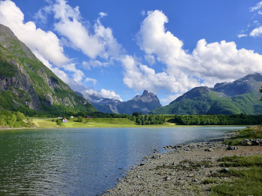 montagne verdi accanto al lago sotto il cielo blu e le nuvole bianche durante il giorno