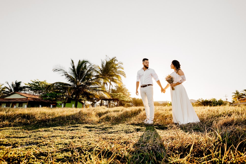 homme et femme en robe de mariée blanche marchant sur le champ d’herbe brune pendant la journée