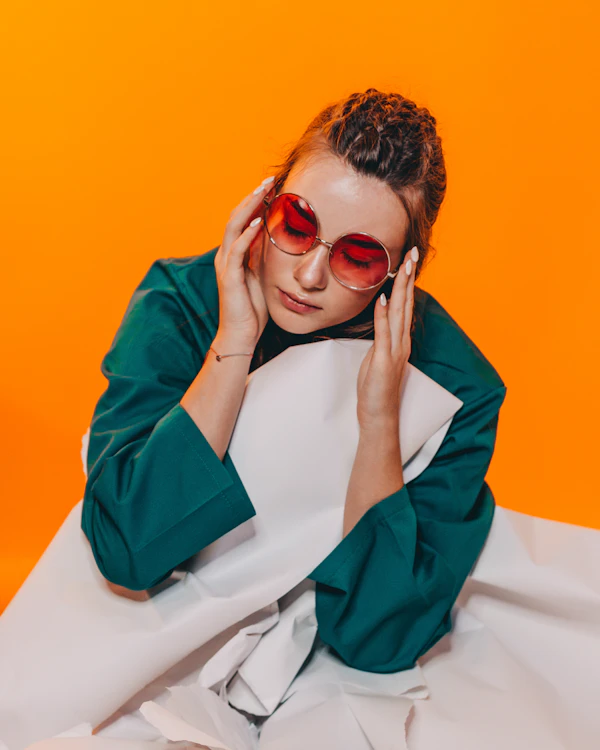 A woman in a green shirt holding orange sunglasses against an orange wall