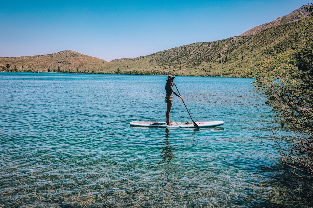 person in black shirt and black shorts riding on white and red kayak on blue sea