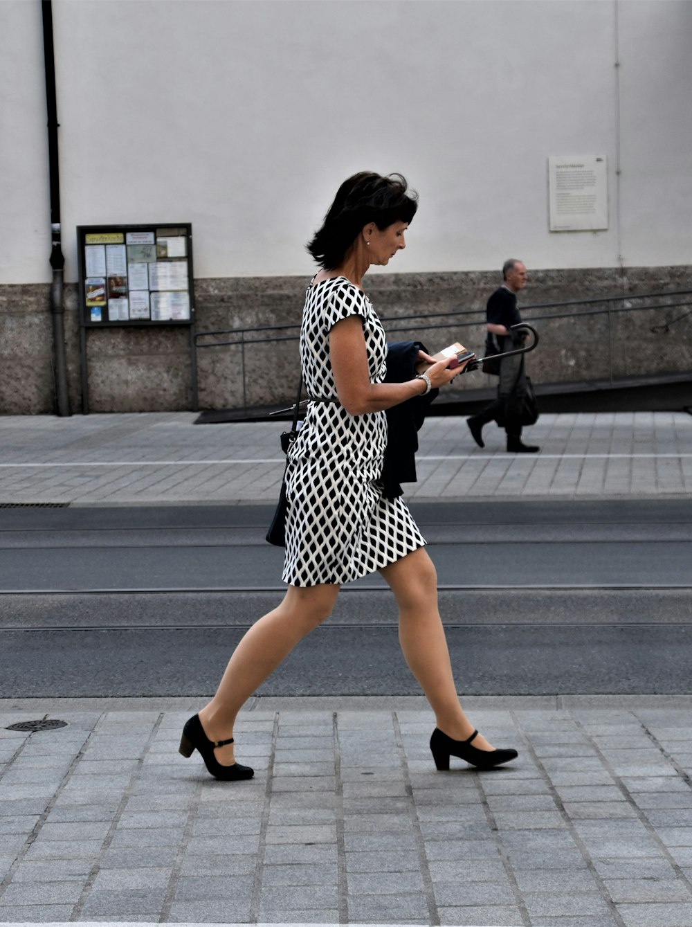 昼間に歩道を歩く黒と白の水玉模様のドレスを着た女性