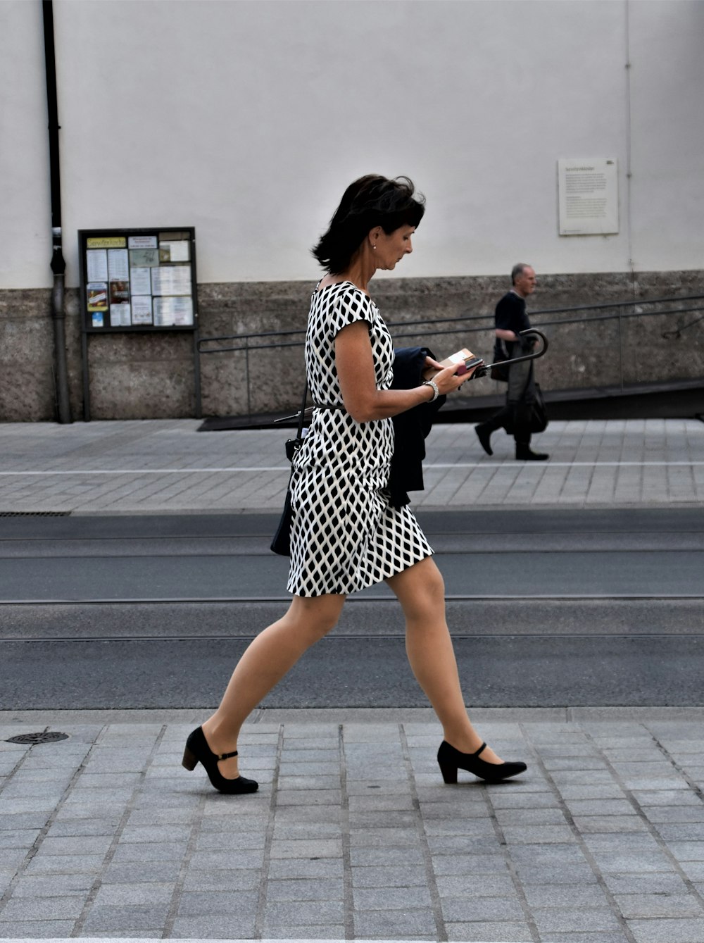 femme en robe à pois noirs et blancs marchant sur le trottoir pendant la journée