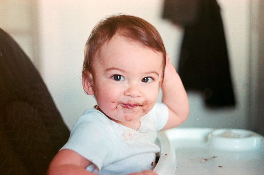 baby in white onesie sitting on white high chair