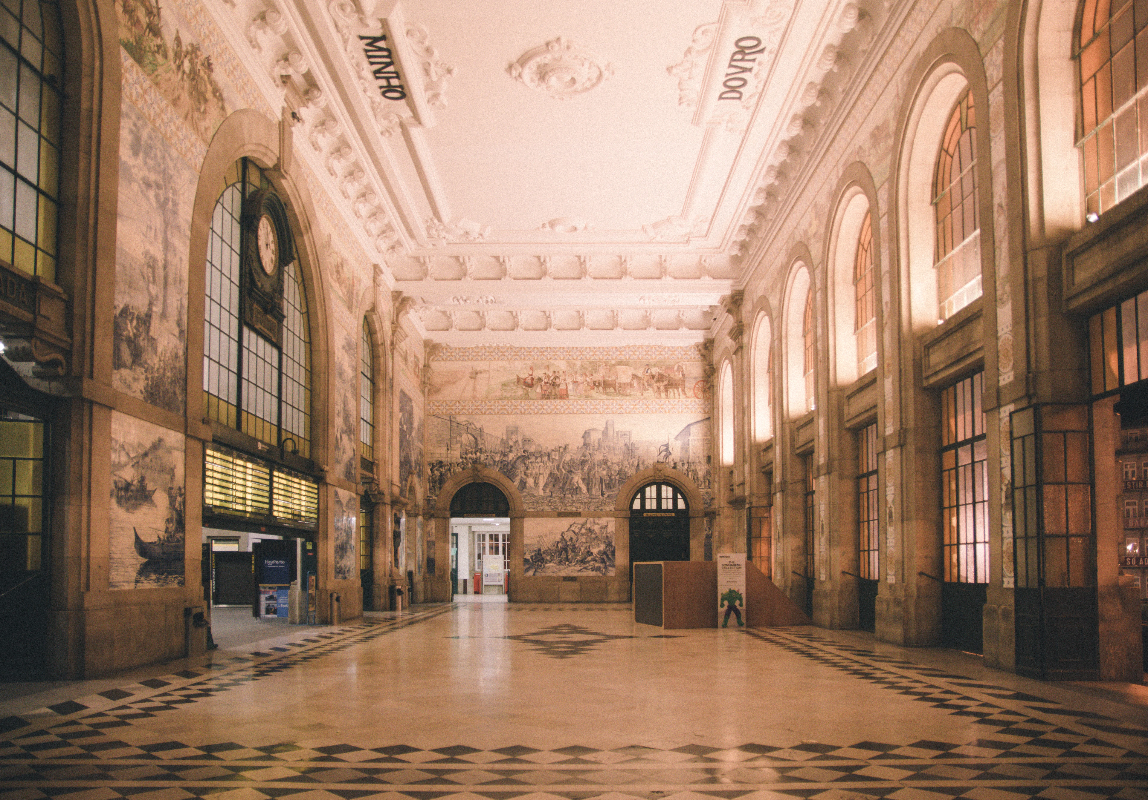 The vaulted atrium of Sao Bento railway station in Porto, its walls covered floor to ceiling in blue-and-white azulejo murals, with warm afternoon light falling across the chequered marble floor.