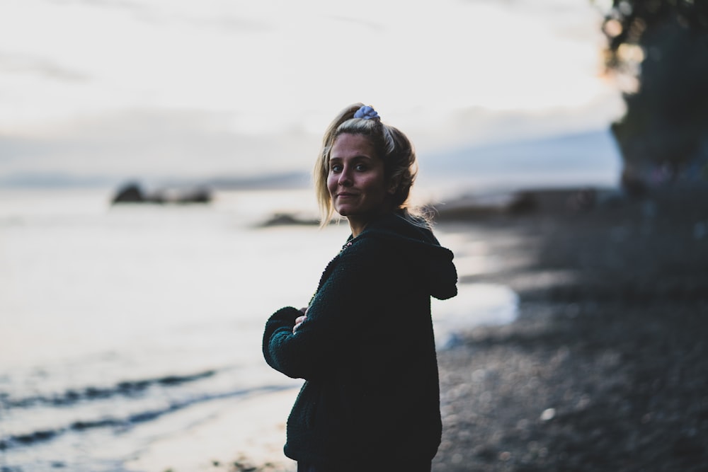 woman in black coat standing on beach during daytime