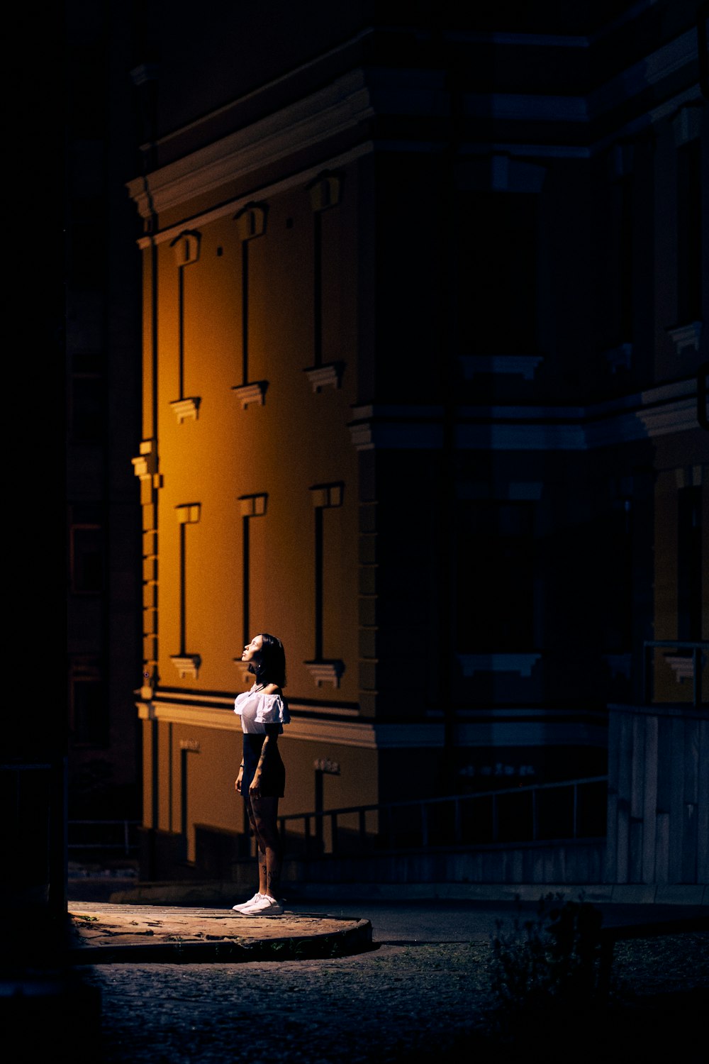 man in white shirt and black pants standing on sidewalk during night time