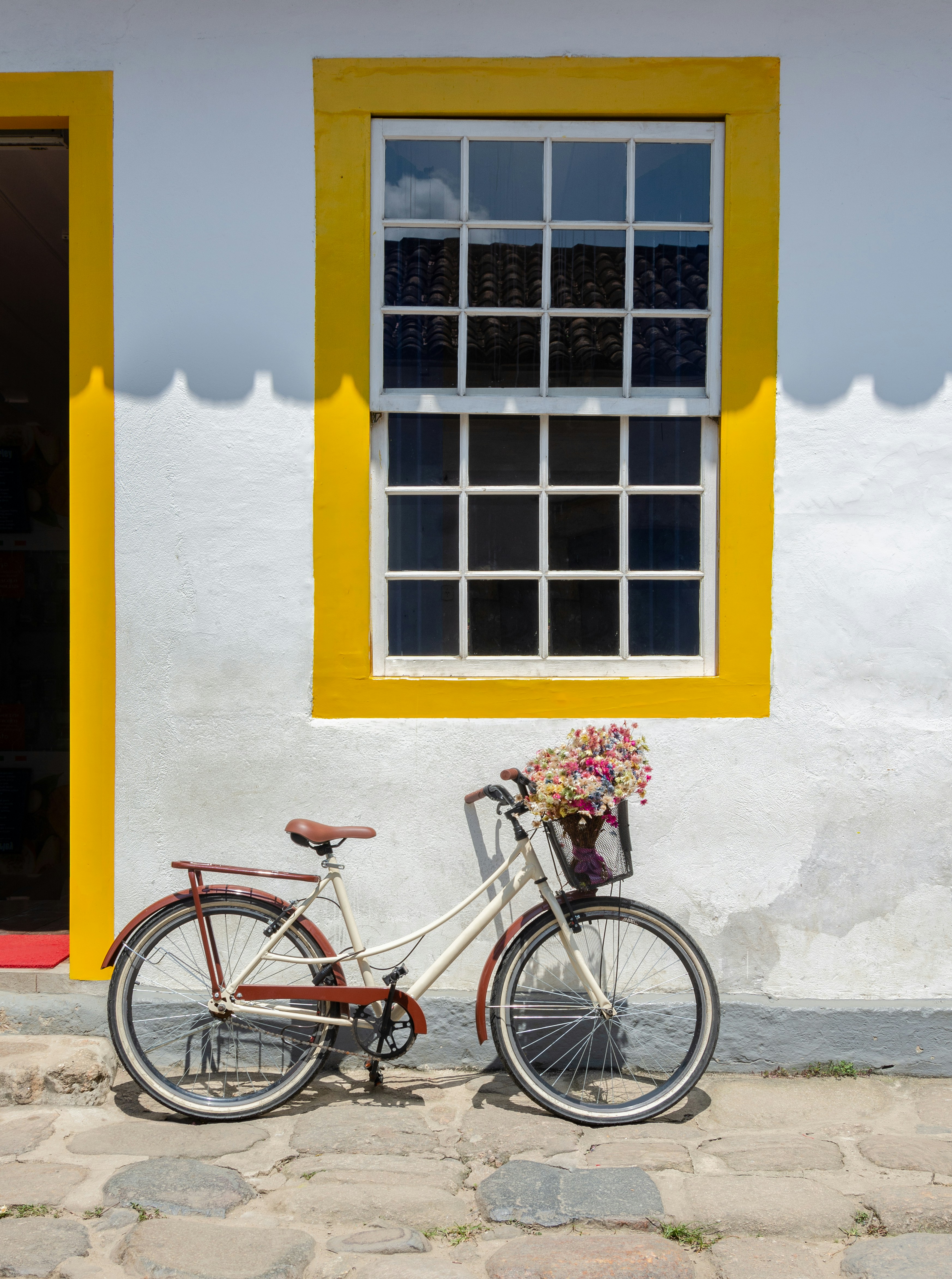 Beautiful bicycle with flowers parked in front of a yellow window in the historic city of Paraty, Brazil.