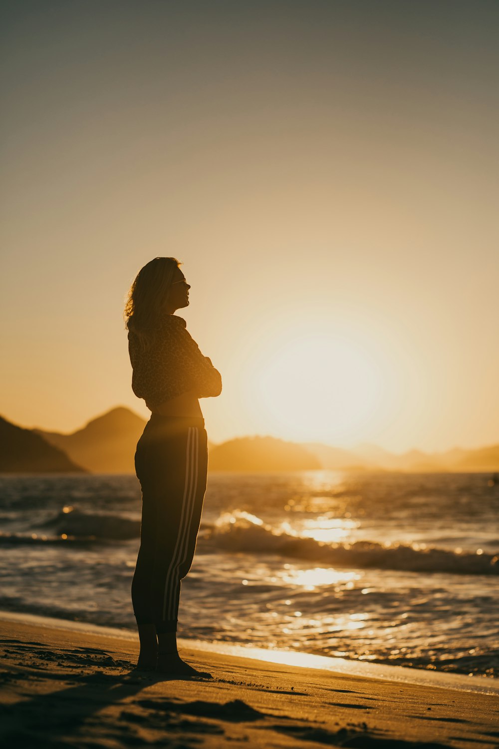 Silhouette einer Frau, die während des Sonnenuntergangs am Meeresufer steht