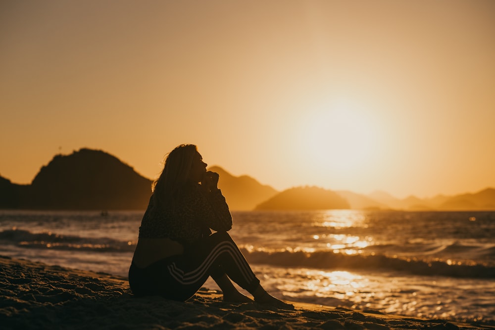 Silhouette einer Frau, die während des Sonnenuntergangs am Strand sitzt