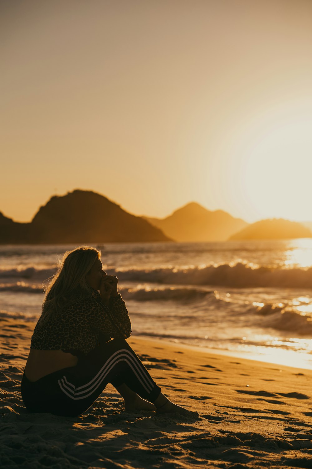 donna in abito bianco e nero che si siede sulla spiaggia durante il tramonto