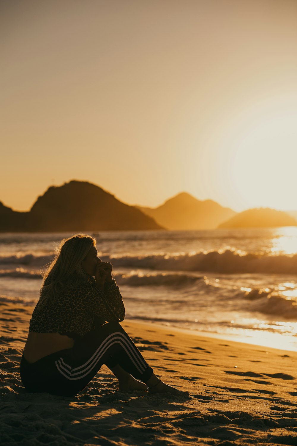 Frau in schwarz-weißem Kleid sitzt bei Sonnenuntergang am Strand