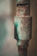 A close-up of an old, rusted metal pipe with visible inscriptions and patches of green and brown corrosion.