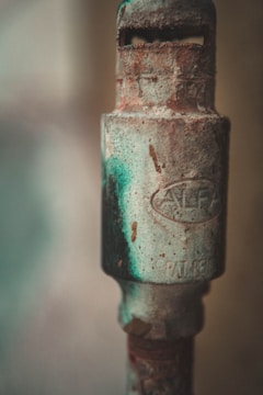 A close-up of an old, rusted metal pipe with visible inscriptions and patches of green and brown corrosion.