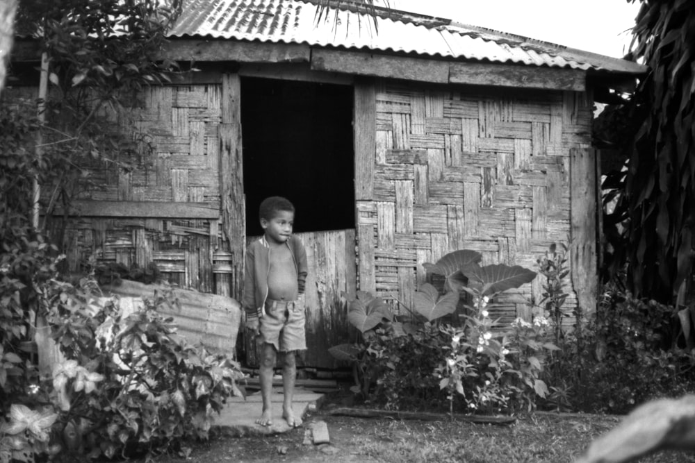 grayscale photo of woman in white long sleeve shirt and black pants standing near brick wall