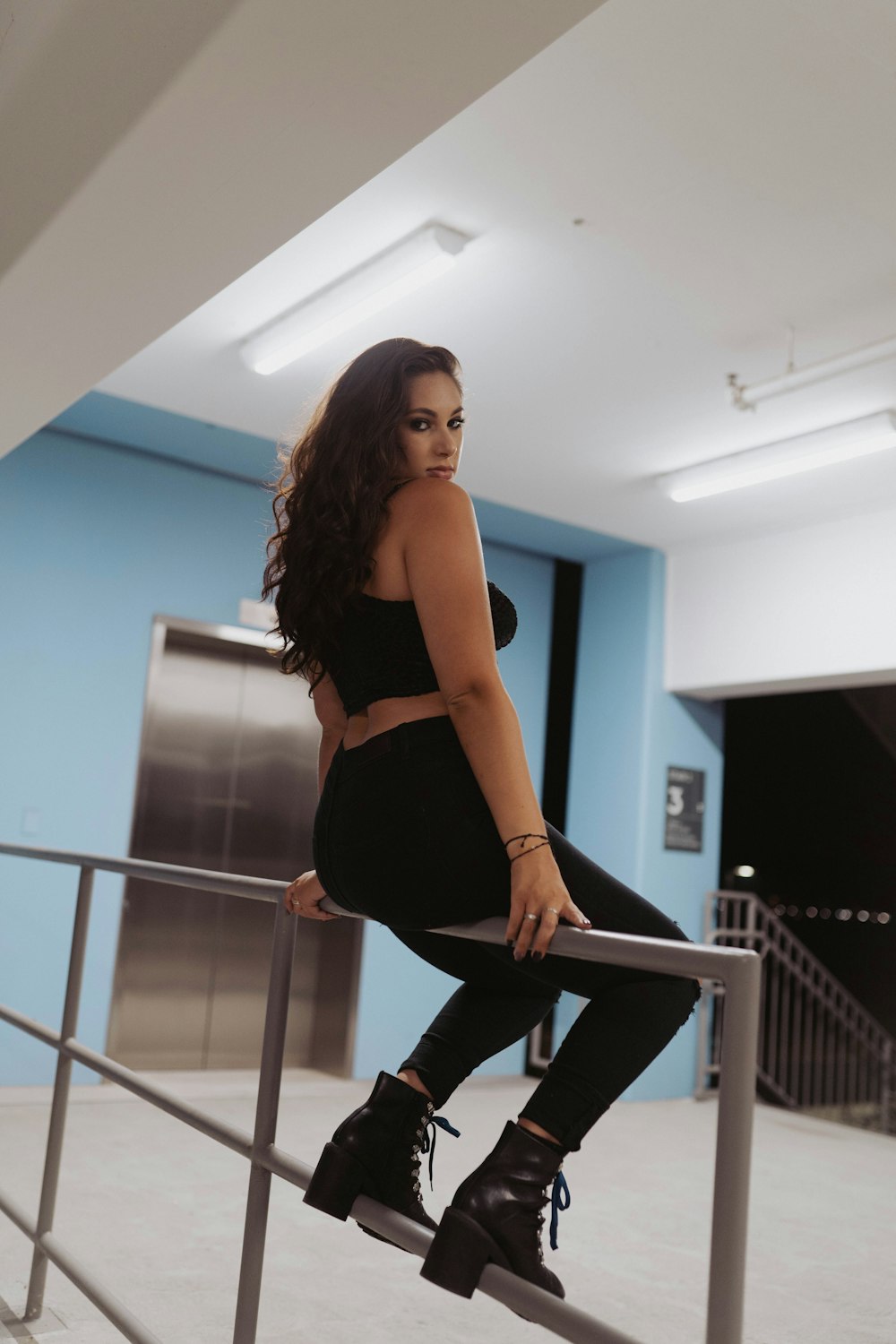 woman in black sports bra and black pants sitting on gray metal railings