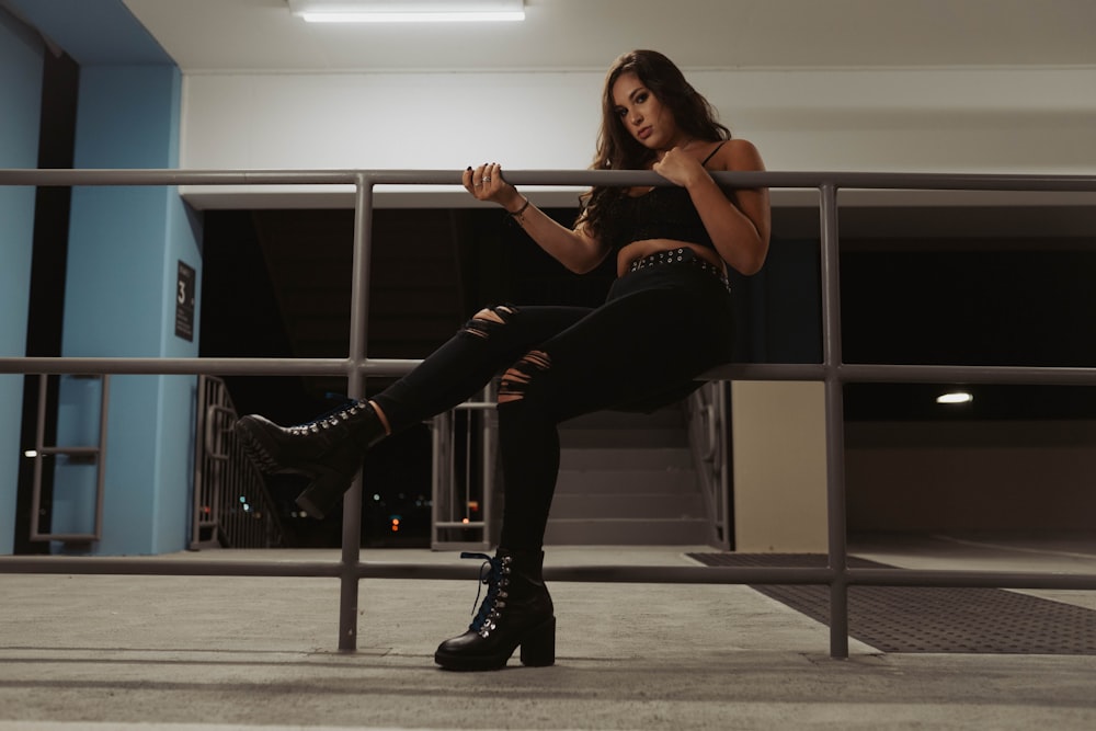 woman in black tank top and black pants sitting on white metal bar