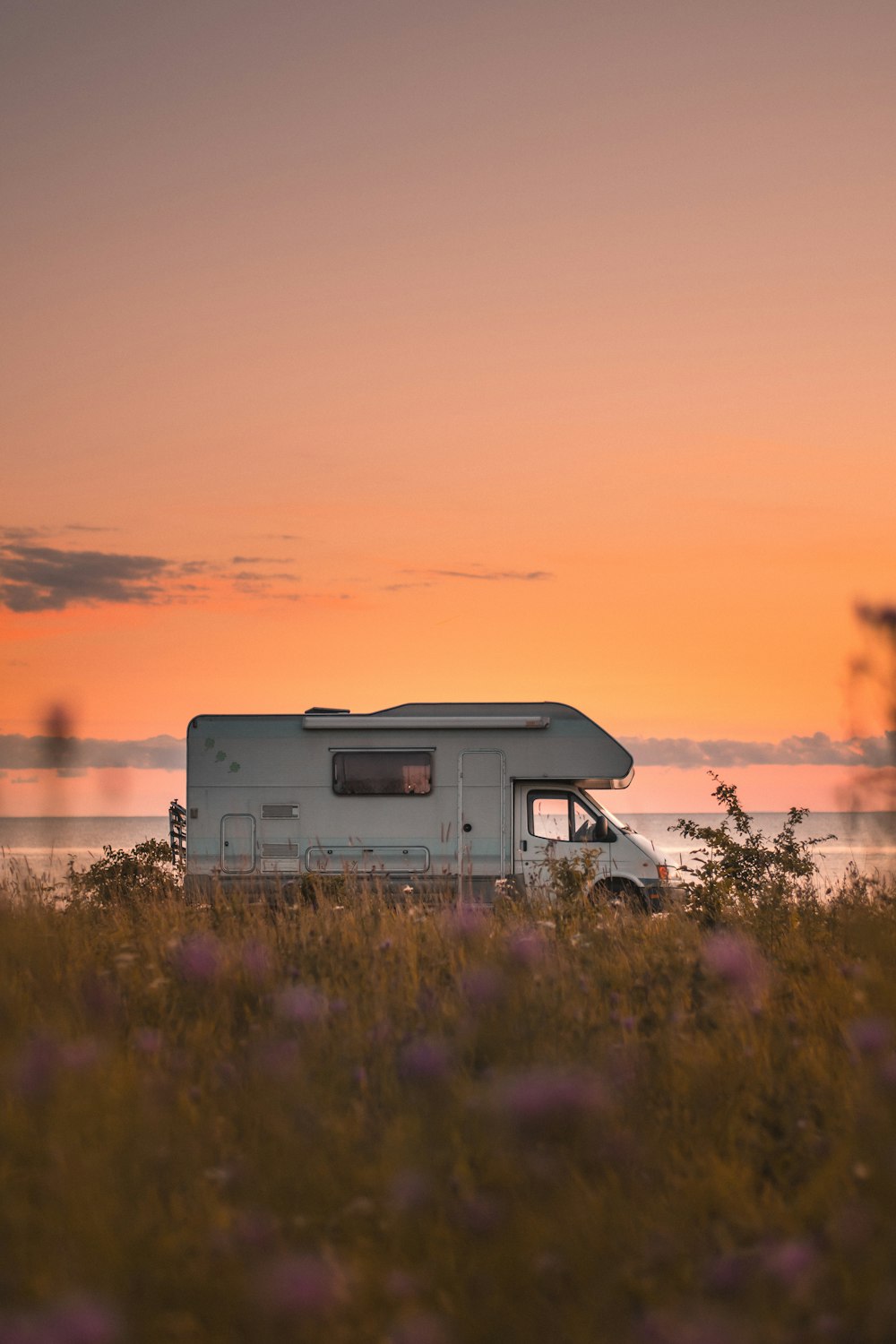 rv branco e cinza no campo de grama verde durante o pôr do sol