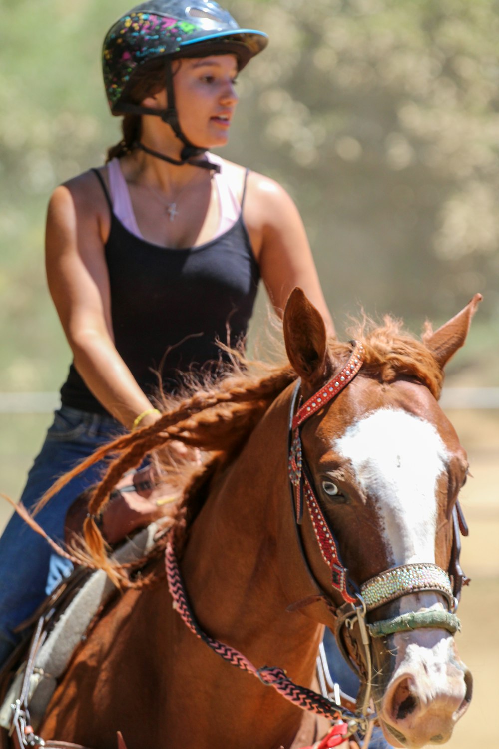 Mujer con camiseta negra sin mangas y jeans vaqueros azules de pie junto a un caballo marrón y blanco durante