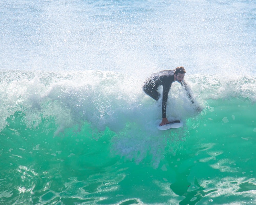 uomo in muta nera che fa surf sulle onde del mare durante il giorno