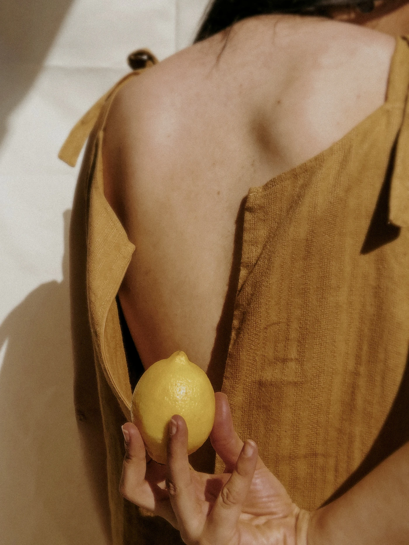 Close-up of an ochre linen top with a hand holding a lemon