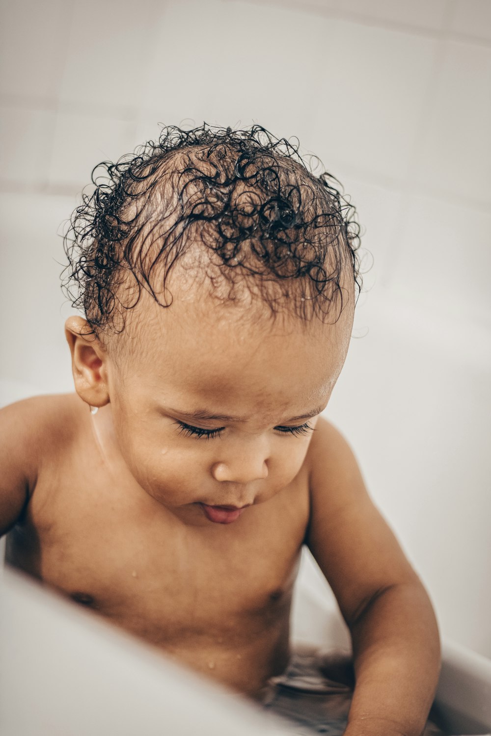 topless baby lying on white bathtub