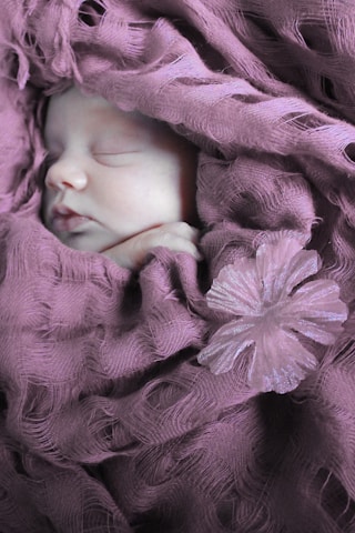 Close-up of newborn baby wrapped in soft fabric.