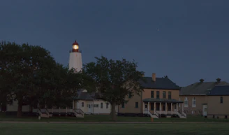 Golden rays of lighthouse light cutting through a navy blue night sky over a peaceful harbor.