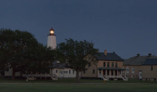 Golden rays of lighthouse light cutting through a navy blue night sky over a peaceful harbor.
