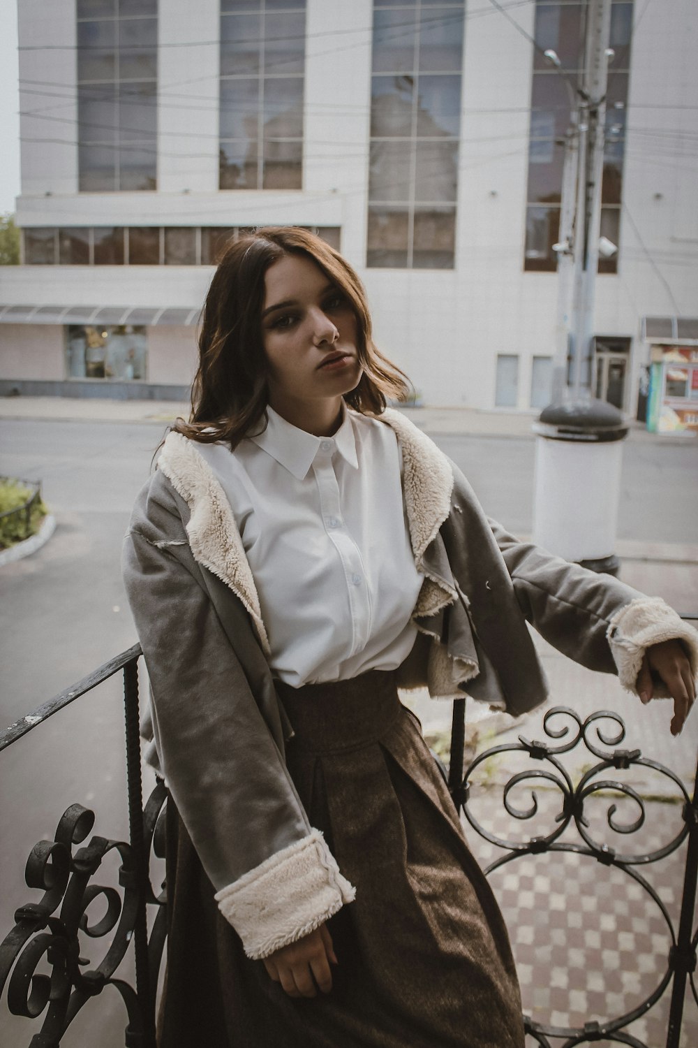 woman in white button up shirt and black jacket sitting on black metal railings during daytime