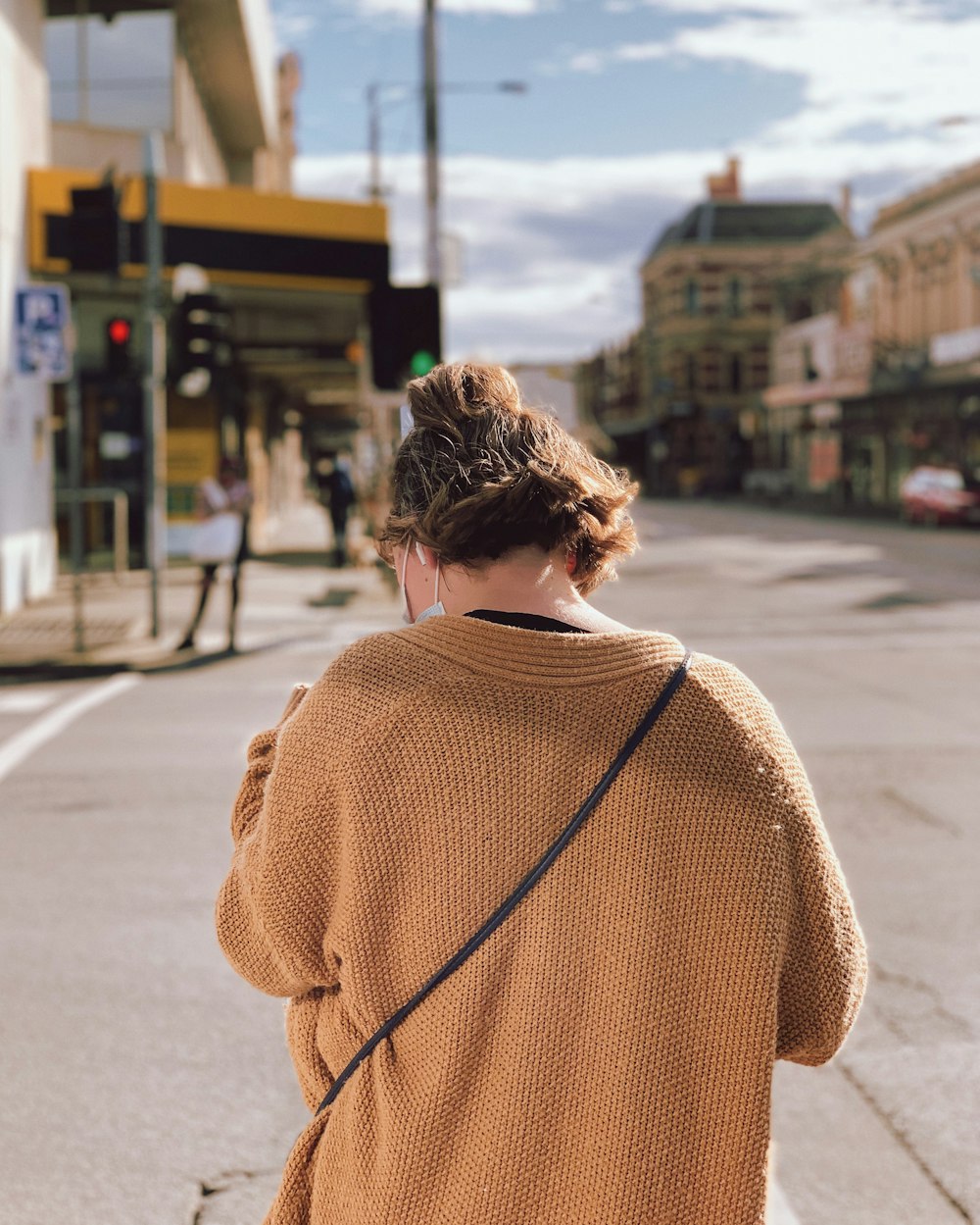 Frau im braunen Strickpullover steht tagsüber auf dem Bürgersteig