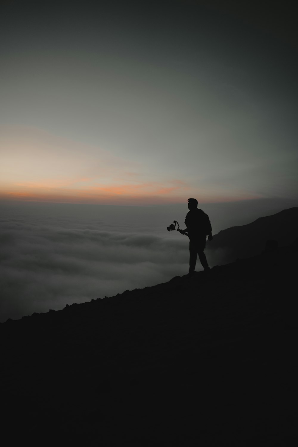 silhouette of man and woman standing on rock formation during sunset