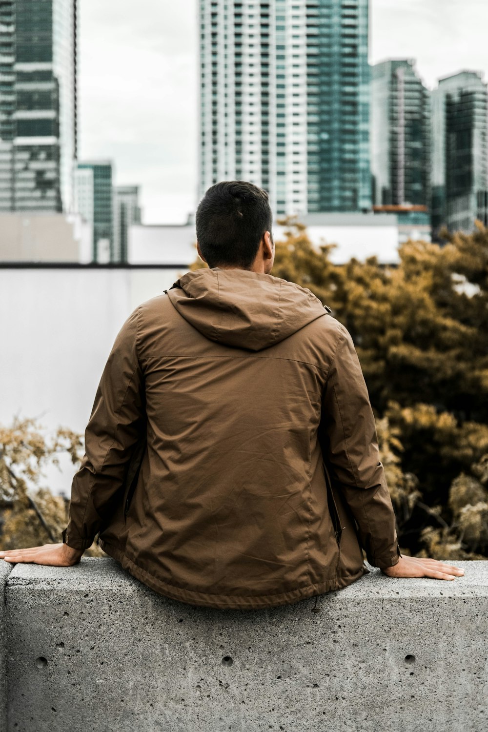 man in brown jacket sitting on gray concrete floor during daytime