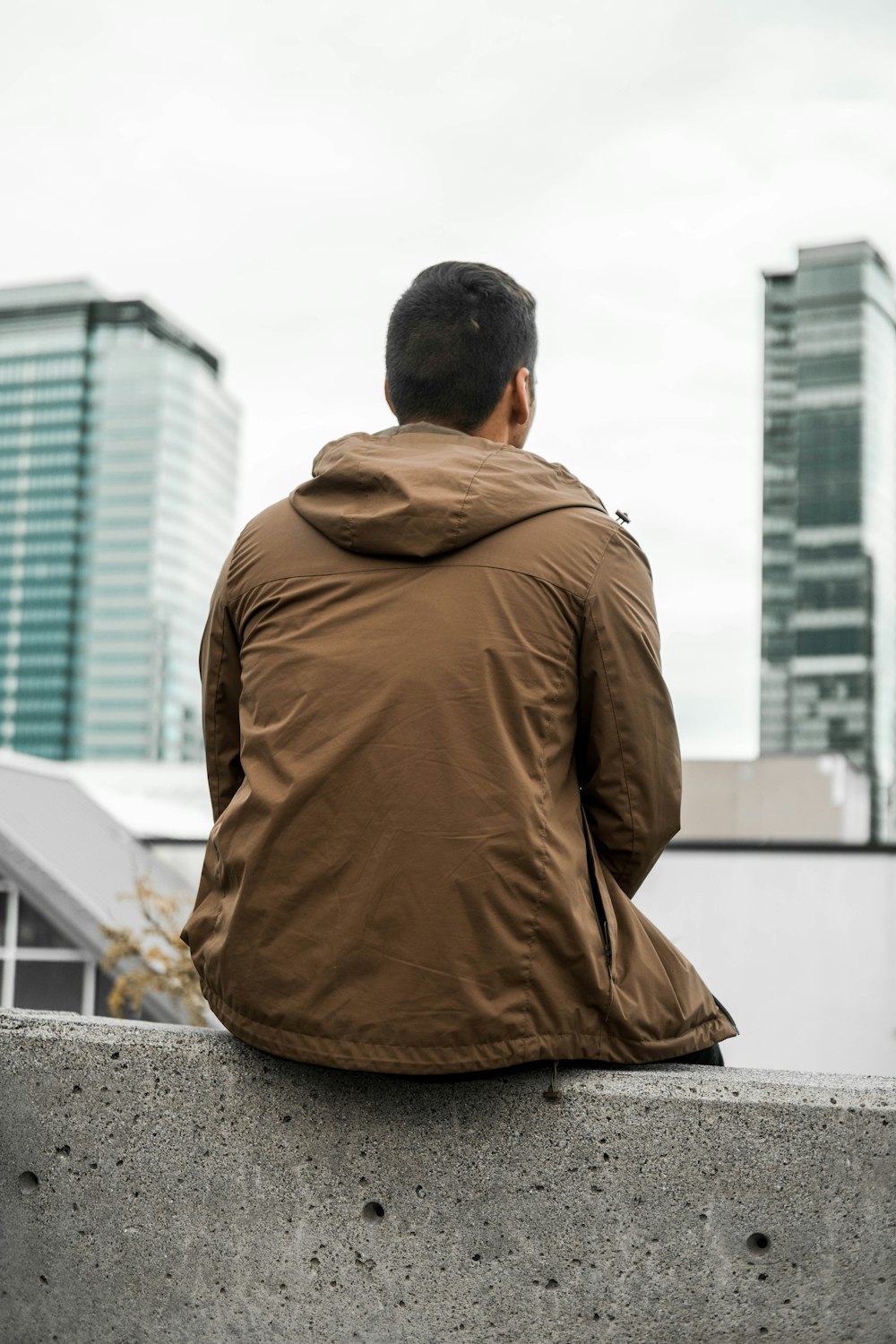 man in brown jacket sitting on concrete bench during daytime