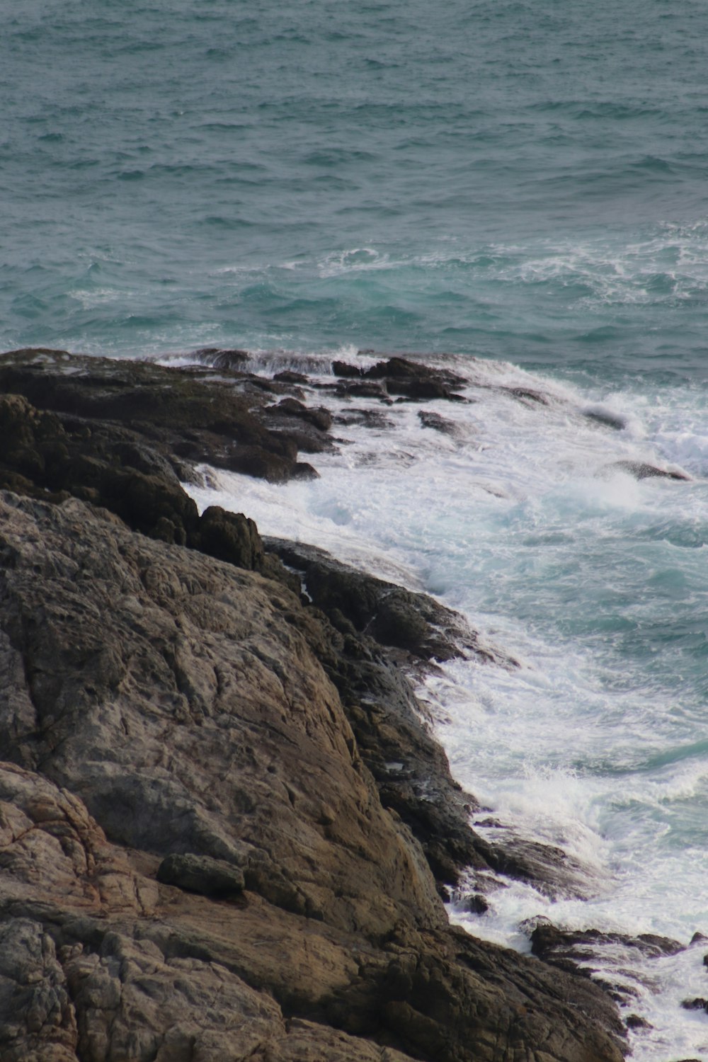 昼間に海の波が岸に打ち寄せる茶色の岩だらけの海岸