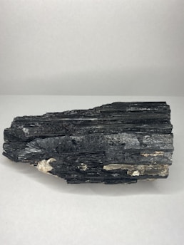 A large black mineral sample with a layered structure and shiny surface, resting on a plain white background. The rock has some lighter brown and white inclusions.