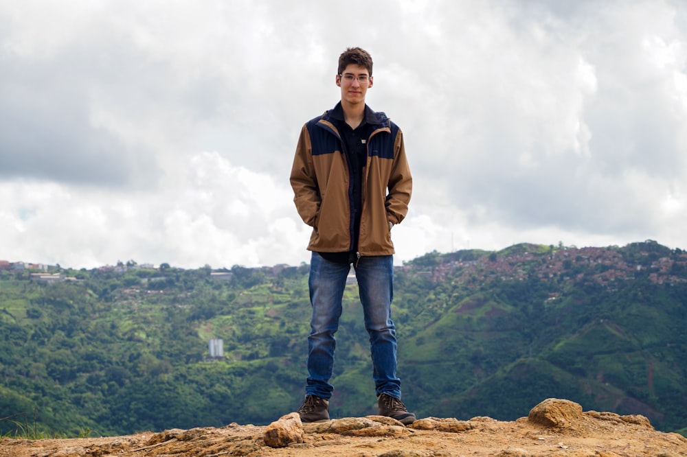 man in brown jacket standing on brown rock during daytime